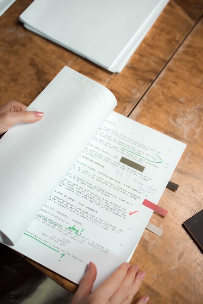 Getting closer... Person's hands holding script pages with handwritten notes on a wooden table.